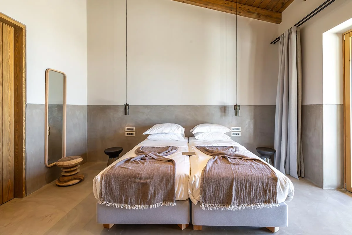 Twin beds with wood ceiling, pendant lights, and soft throws in a calming room at Eliamos hotel in Kefalonia.