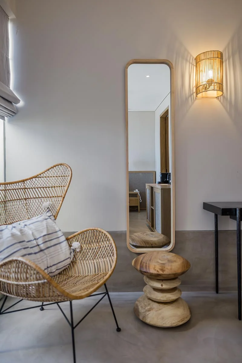 Cosy corner with wicker chair, striped pillow, and full-length mirror in an Eliamos suite.