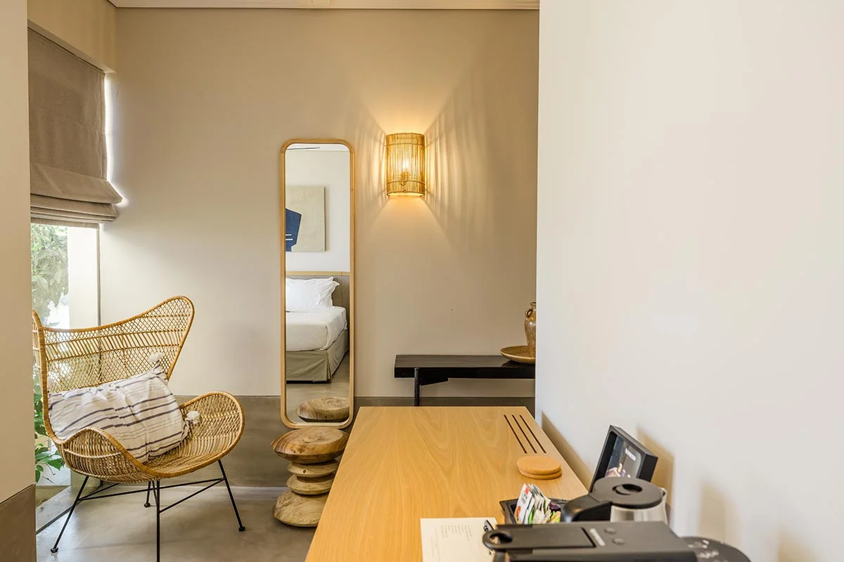 Wicker chair and wooden desk in a serene room with mirror and neutral tones at Eliamos in Kefalonia.