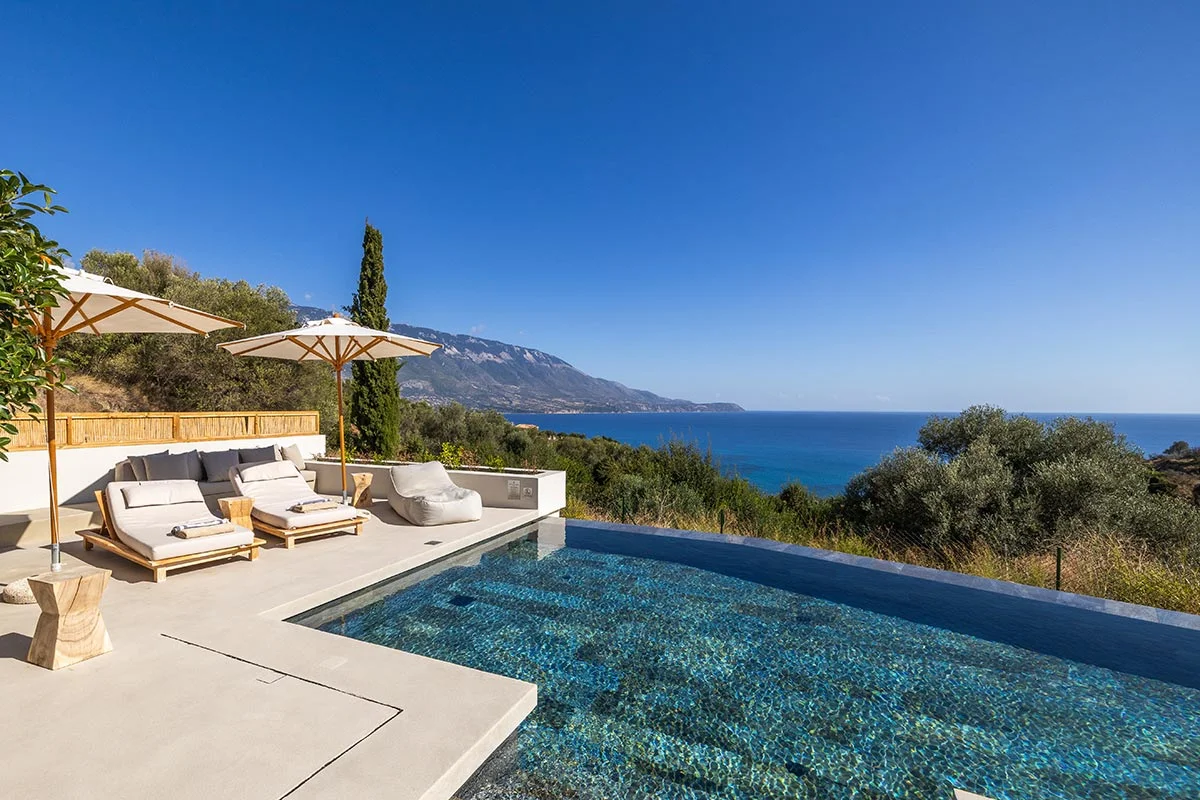 Infinity pool at Eliamos in Kefalonia with sunbeds, umbrellas and panoramic views over the Ionian Sea.
