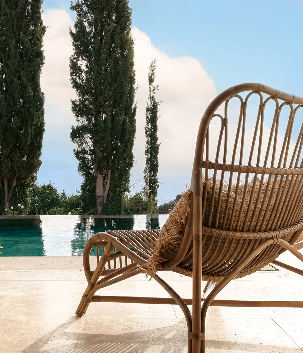 Rattan chair by the infinity pool with cypress trees and sea view at Eliamos luxury resort in Kefalonia, Greece.
