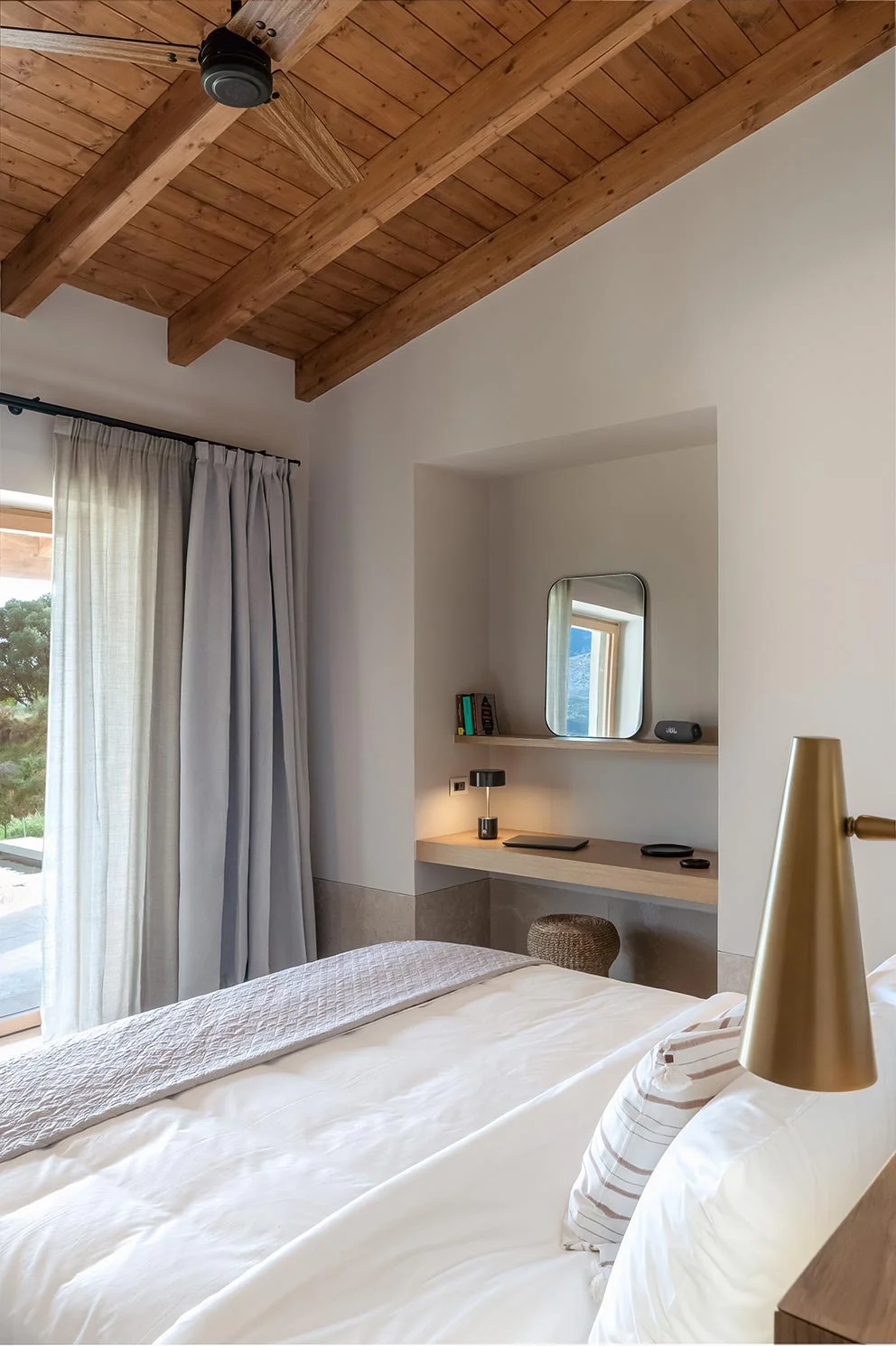 Bedroom with wood-beamed ceiling and built-in desk overlooking the garden at Eliamos wellness resort in Kefalonia.