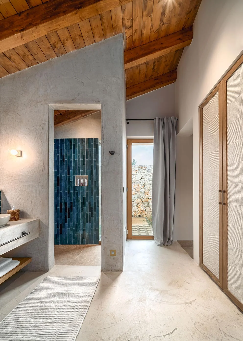 Bathroom at Eliamos resort in Kefalonia with natural plaster walls, vaulted wooden ceiling and dark blue tiles.