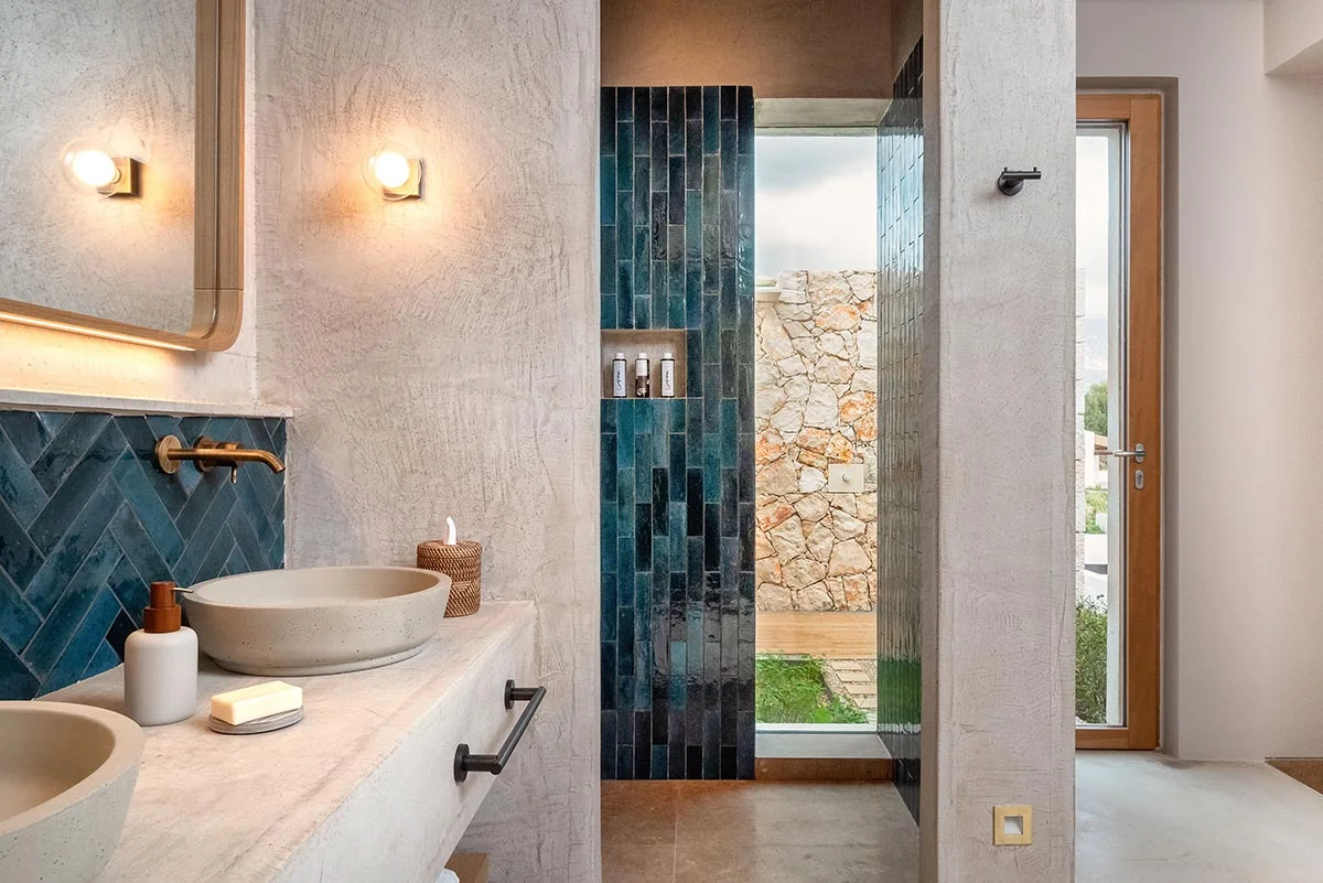 Vanity with stone sinks and deep green tiled shower wall in natural light at Eliamos in Kefalonia, Greece.