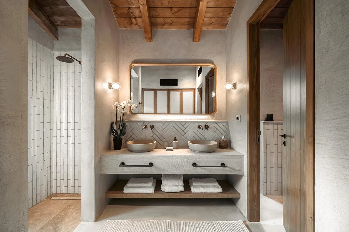 Rustic-style bathroom with twin stone sinks, wood ceiling, and walk-in shower at Eliamos resort in Kefalonia.