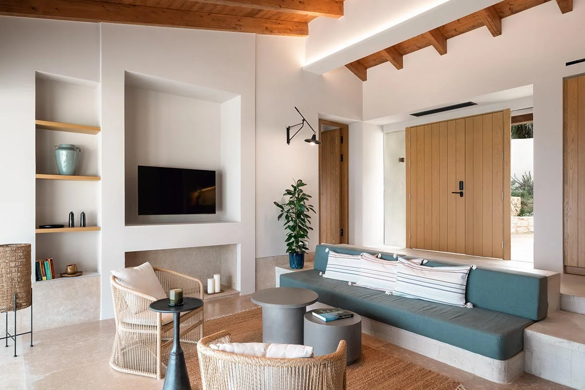 Minimalist living area with wood beam ceiling, built-in sofa and TV at Eliamos in Kefalonia, Greece.