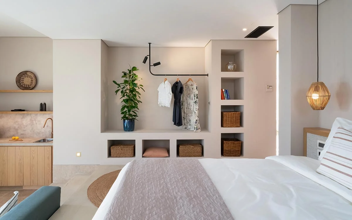 Bright bedroom with open wardrobe, indoor plant, and compact kitchenette at Eliamos in Kefalonia, Greece.