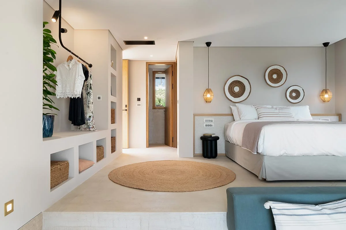 Minimalist Eliamos bedroom in Kefalonia with built-in open wardrobe, round rug, soft lighting and woven baskets.