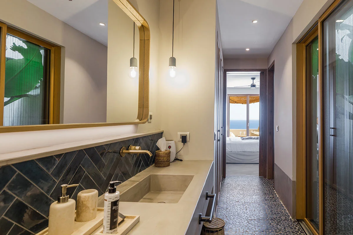 Modern Eliamos bathroom in Kefalonia with long mirror, pendant lights, and view into the bedroom and sea.
