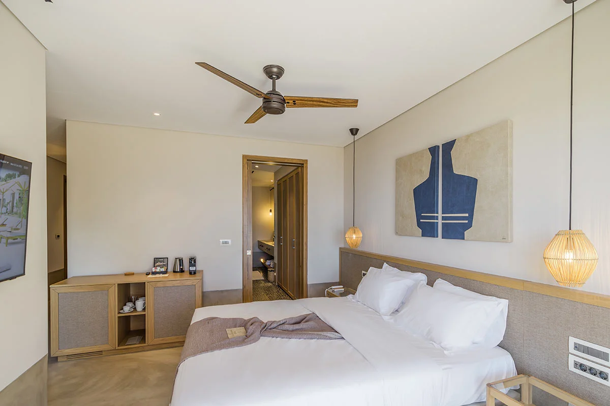Elegant bedroom with king bed, ceiling fan, and modern artwork in a suite at Eliamos luxury resort in Kefalonia.